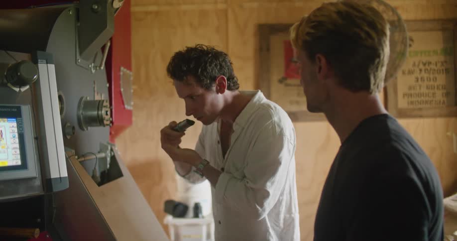 Two men smell the aroma of coffee beans from an industrial roaster