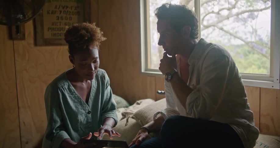 A man and woman at home talk as he hands her a tablet to look at