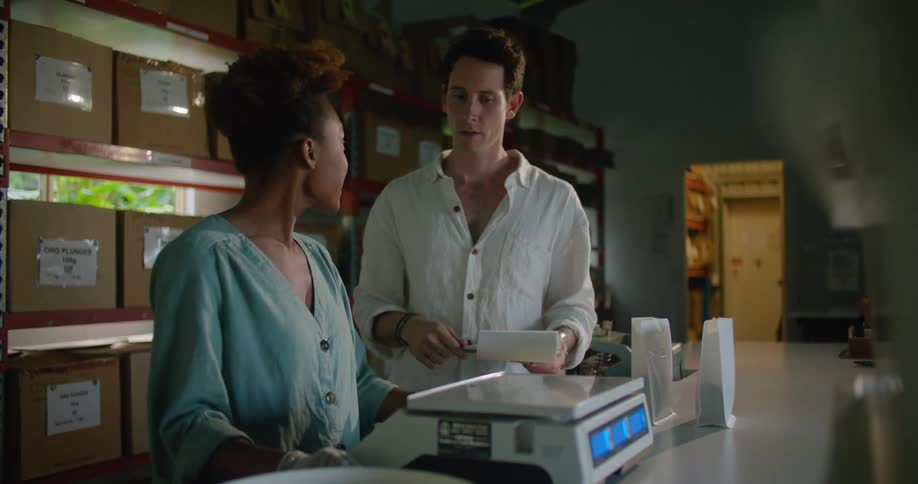 A man holding a clipboard talks with a woman standing at a counter with a scale