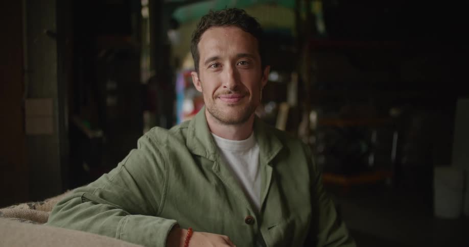 A man takes a sip of coffee and smiles while posing against a table