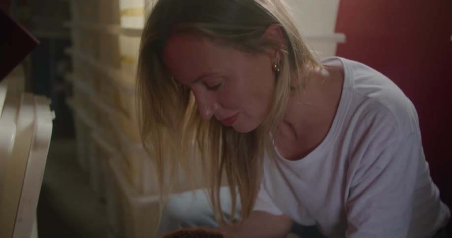 Blonde woman with white t shirt and jeans smells coffee beans in coffee warehouse