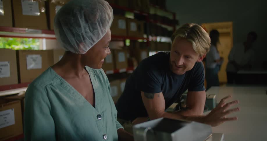 A man leans on a counter and talks with a woman wearing a hair net using a food scale