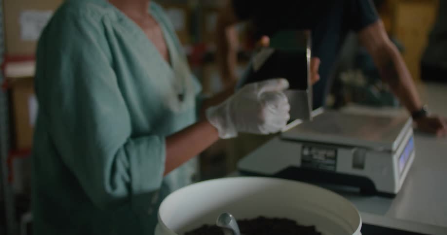 A man talks to a woman as she scoops weighs and bags coffee beans