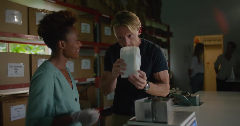 A woman pours a scoop of coffee beans into a bag then she and a man smell the aroma