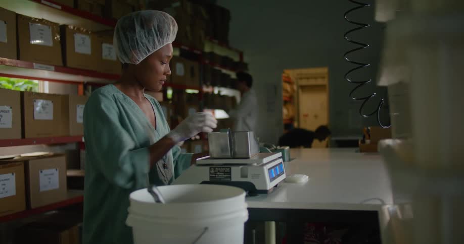 A woman weighs fresh roasted coffee beans on a scale then pours them into a bag