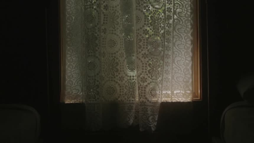 A dark room has a window with a curtain