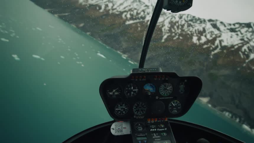 Male pilot operates helicopter over sea with glaciers next to high snowy mountain