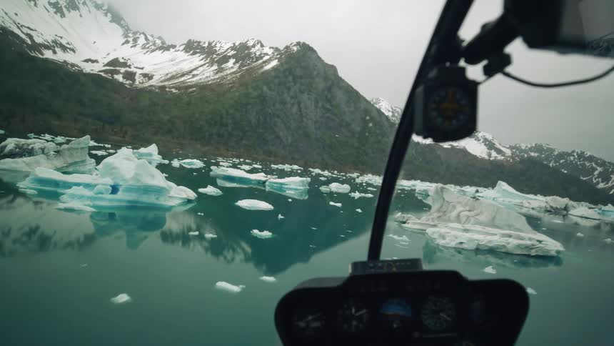 A helicopter flies close to the surface of a body of water covered with glaciers
