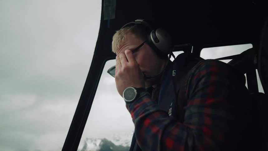 A man wearing sunglasses and a head set is piloting a helicopter