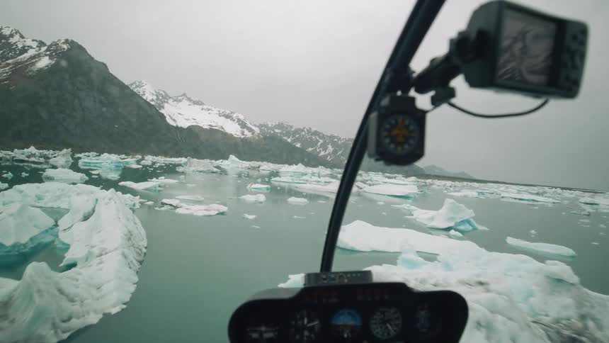 Aerial view from the cockpit of an helicopter flying over the icebergs on the ocean near the mountains