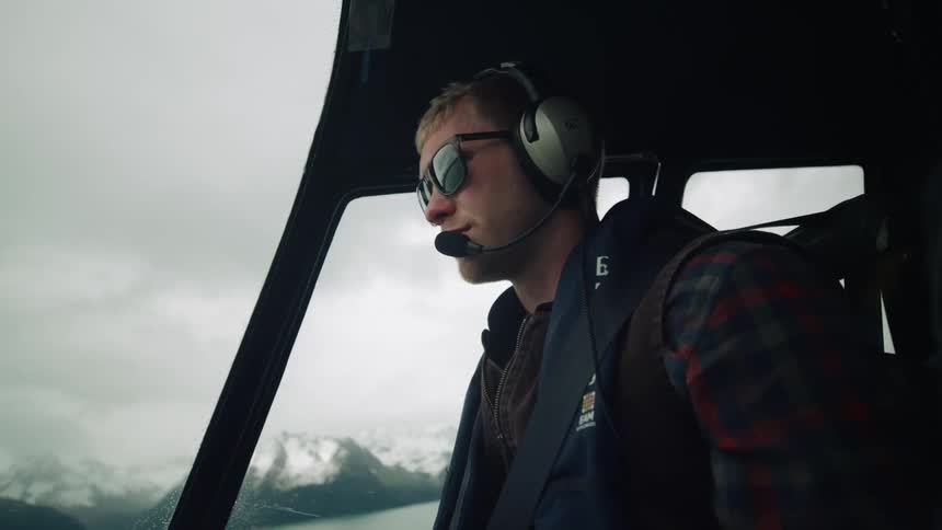 A man wearing a headset and sunglasses is flying a helicopter