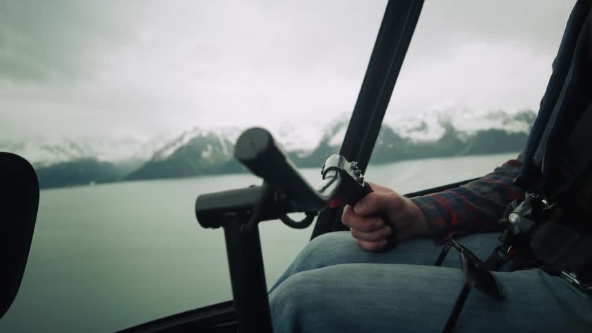 Inside a speeding watercraft a man is sitting and piloting the vessel across a large lake with snow covered mountains in the background on a cloudy winter day