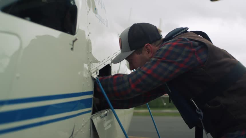 Man uses contents of bottle in area behind access port on side of helicopter