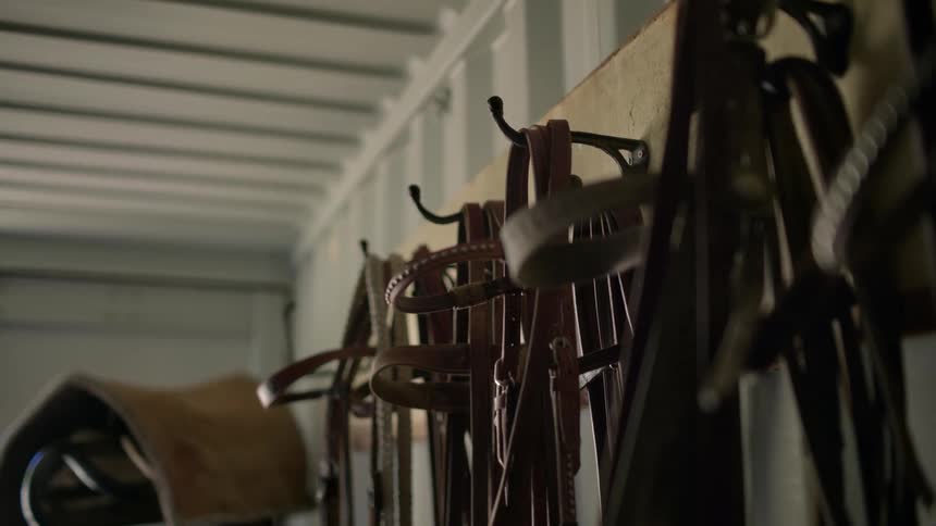 A man grabs riding gear off a hook in a building