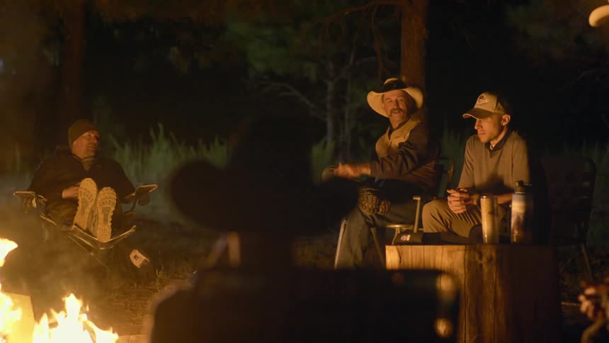Four people are sitting outside at night near a bonfire