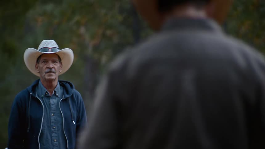 Two men talk outside while wearing cowboy hats