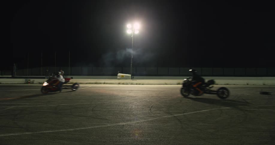 A group of motorcyclists ride in circles on a racing strip at night