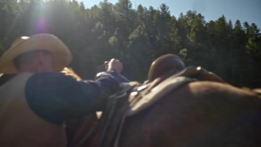 Cowboy carrying a sadle on a corral puts it over a horse
