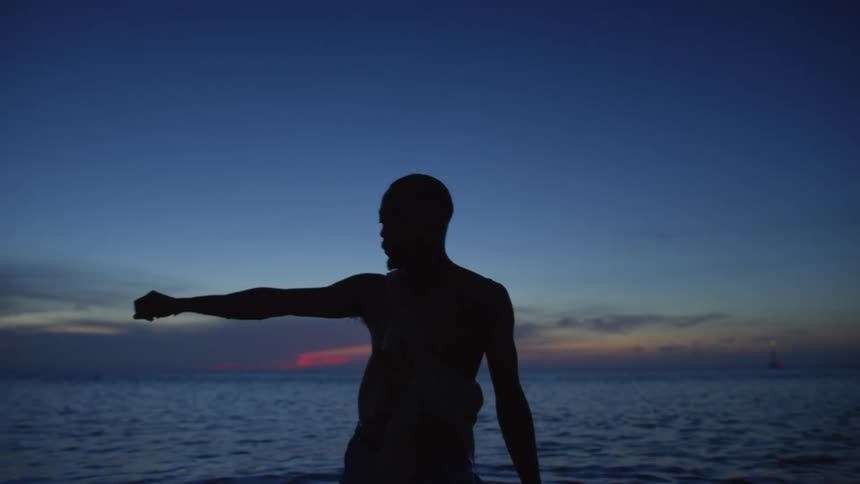 Man stands in ocean water silhouetted against crimson sky on horizon