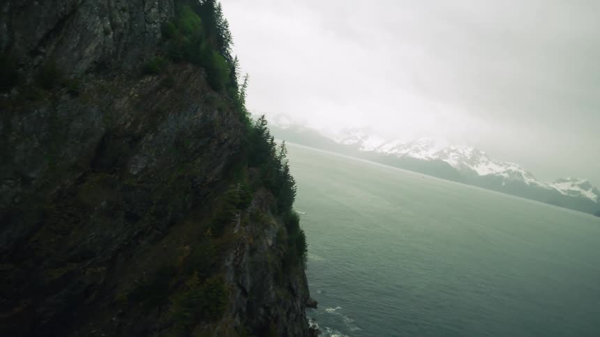 Aerial view of oceanside cliffs with distant snowy mountain range in the background
