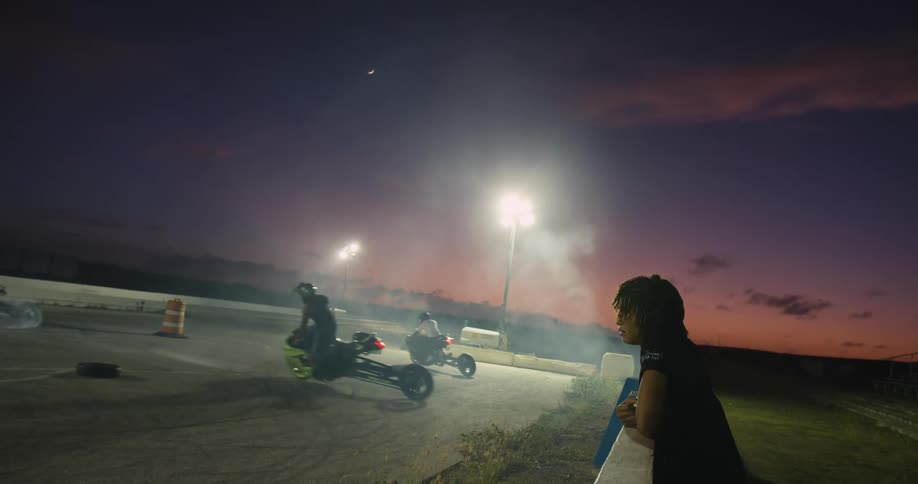 A teenage boy watches people race motorbikes around an arena