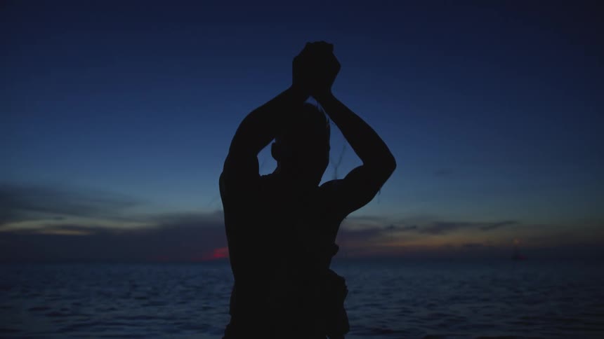 Man silhouetted by light from red horizon rises his hands over his head