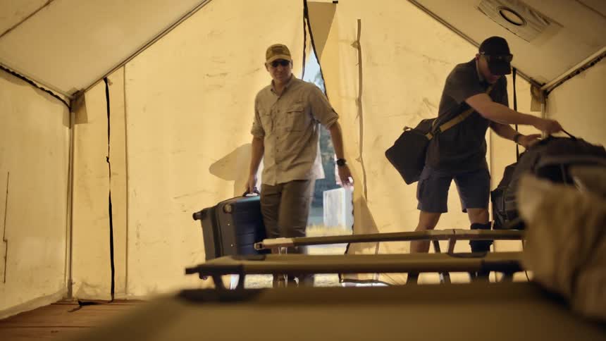 Three men bring their luggage into the large tent