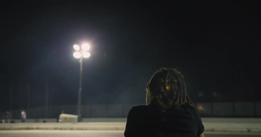 Young man with dreadlocks sitting on an empty racetrack at night