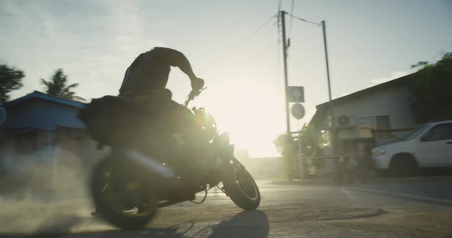 Man spins motorcycle on road kicking up dust