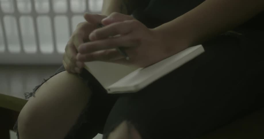 Person sitting and fidgeting with a pen and notebook