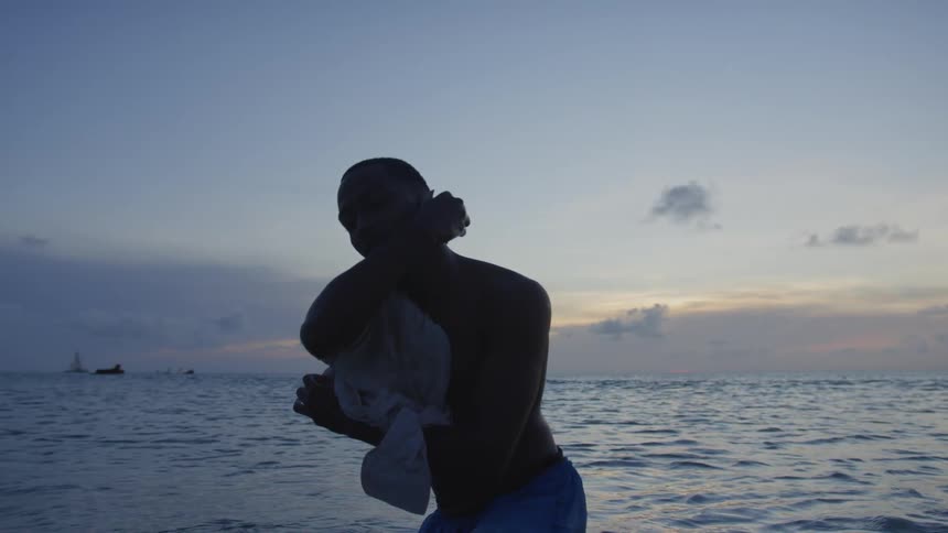 Silhouette of a man standing in the water and moving his shirt around his shoulders