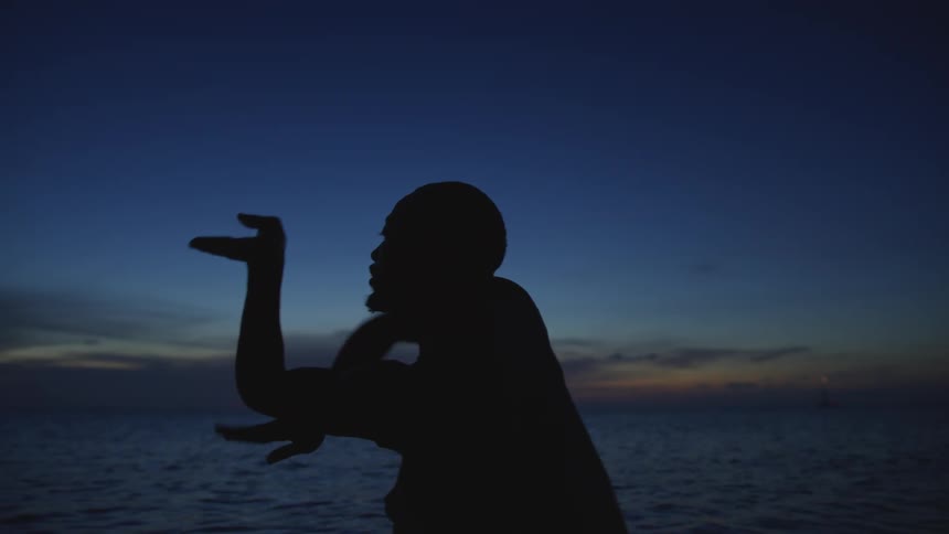 Silhouette of a man standing in the water doing tai chi movements as the sun sets on the horizon