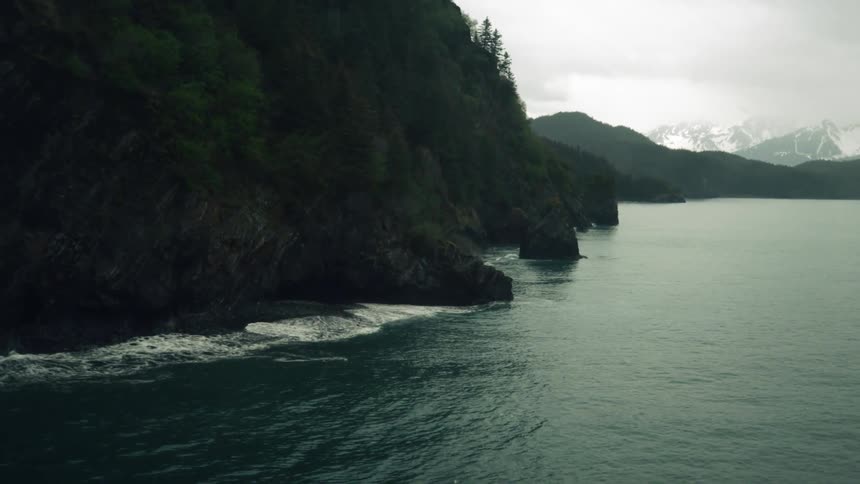Aerial view of ocenside cliffs with distant snowy mountains under the clouds
