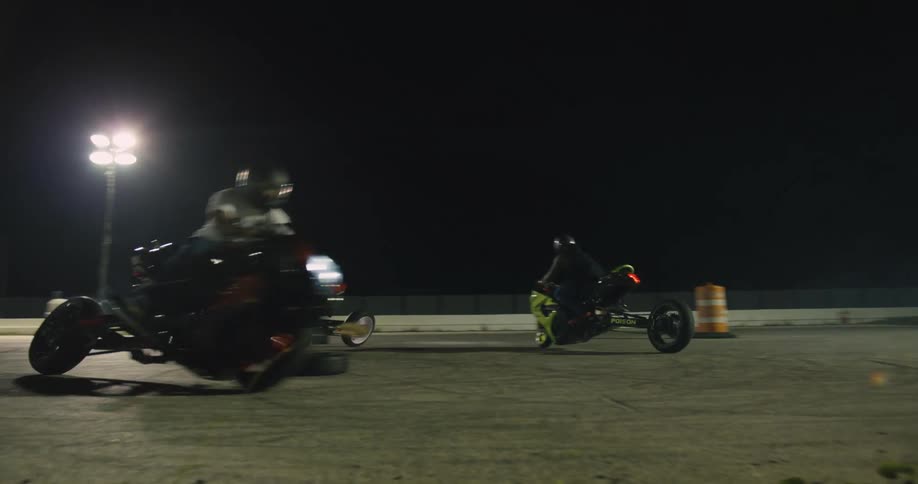 Competitors race motorcycles around track at night