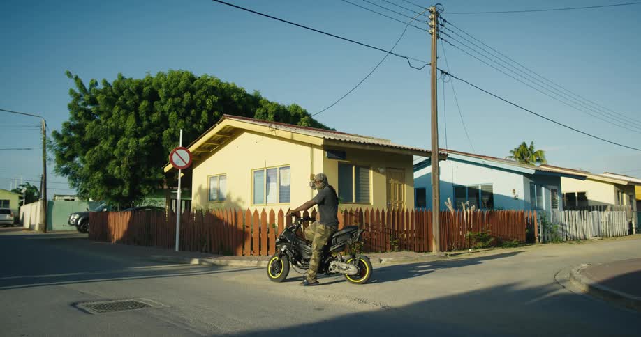 Man wearing mask sits on motorcycle near intersection in neighborhood