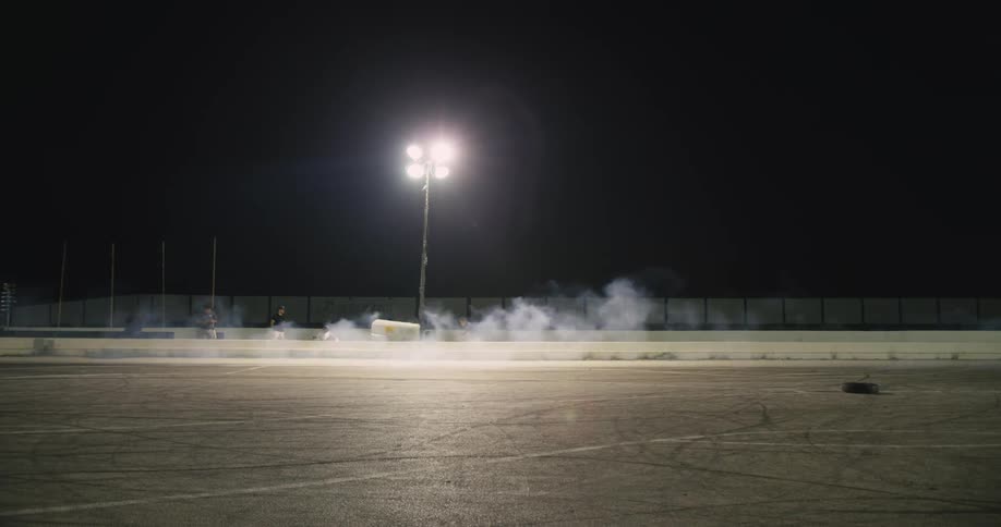 Crew stands behind a barrier as a motorbike passes by on the track leaving a cloud of dust