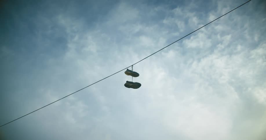 Couple of sneakers hanging from a power line at day