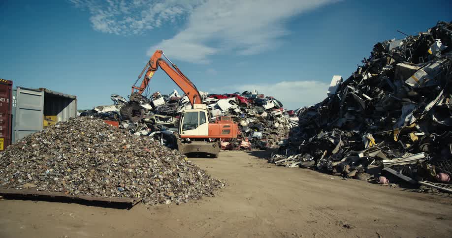 A crane and a bulldozer operate in a junkyard during the day