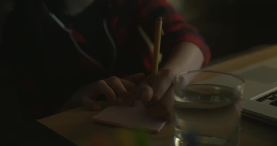 A person writes on a notepad by a laptop