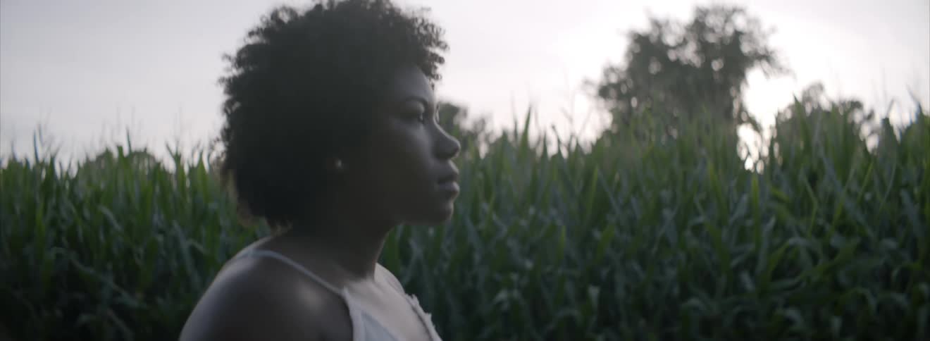 A black woman stands near a cornfield and looks ahead
