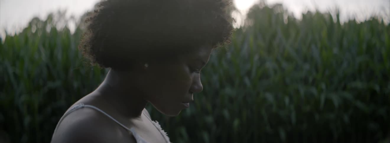 A woman stands outside beside a cornfield
