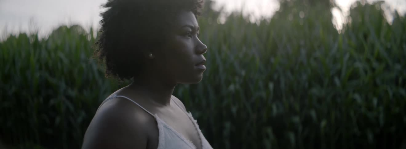 Woman standing by corn field staring off into the distance