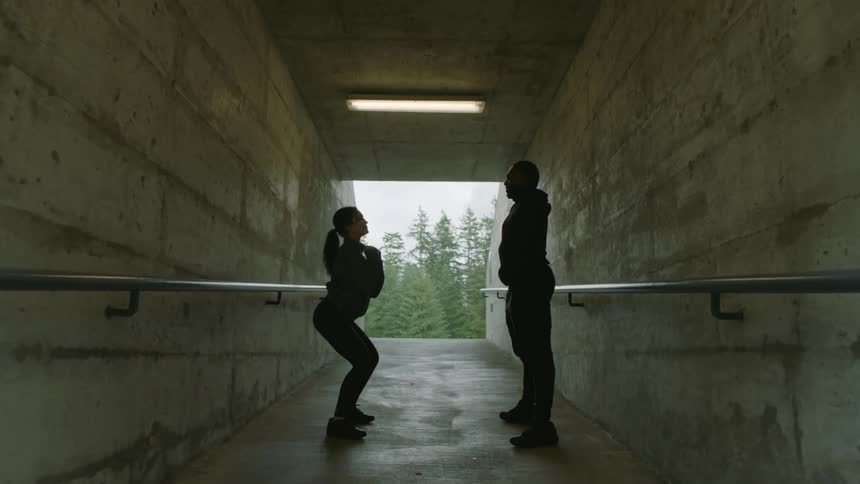 Two friends wearing black clothes stretching on a concrete hallway