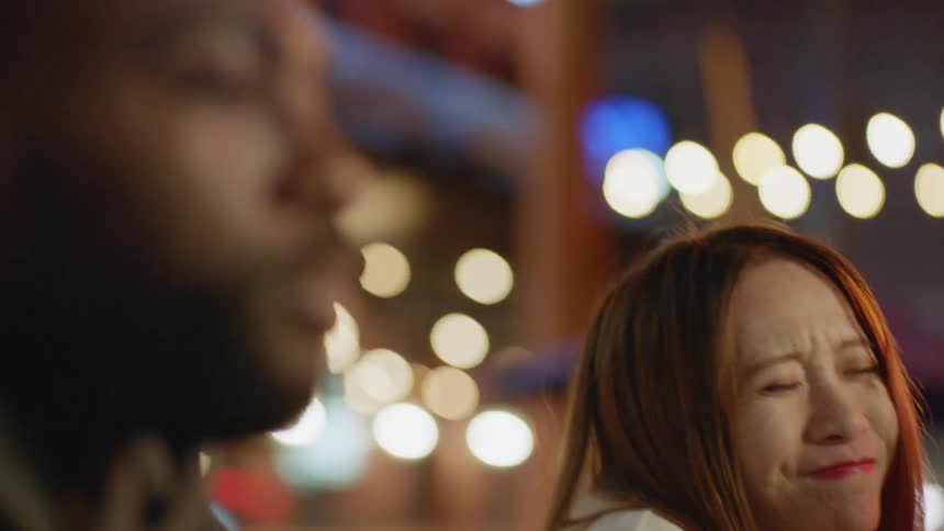 A group of friends eat pizza together an at outdoors table in a city at night