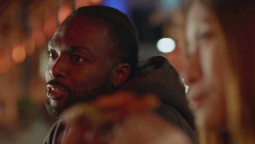 Friends eating pizza on an outdoors restaurant in the city at night