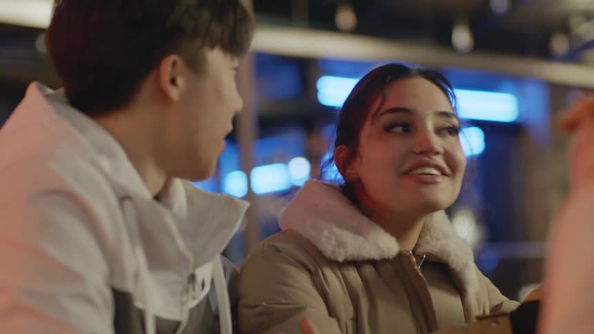 A man and woman are talking as they sit outside and the woman is holding pizza