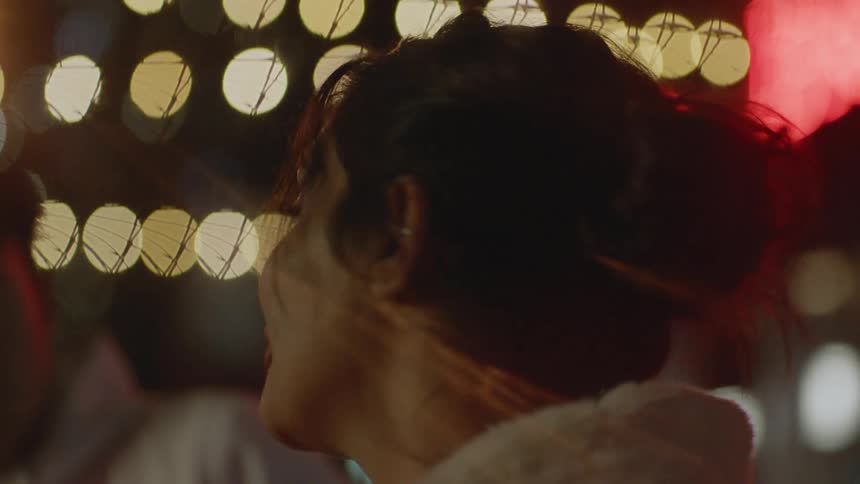 Man and woman smile and talk near brightly lit buildings with neon signs at night