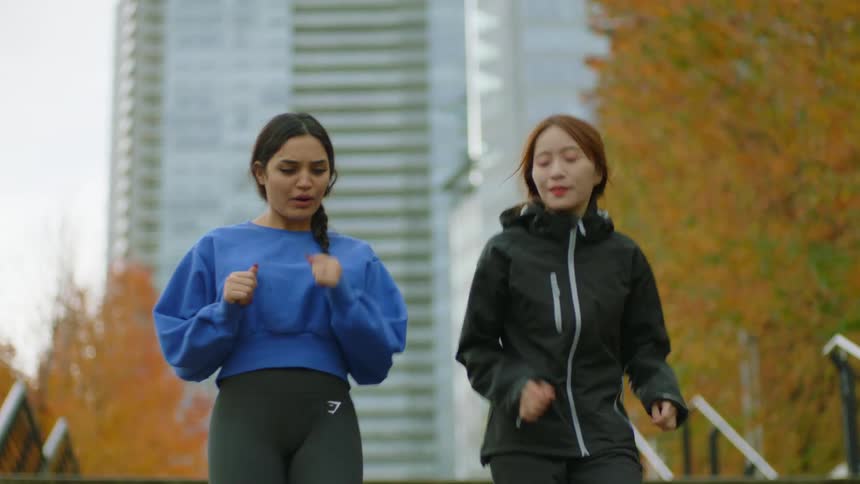 Two friends sitting on a staircase in a park stand up and start jogging