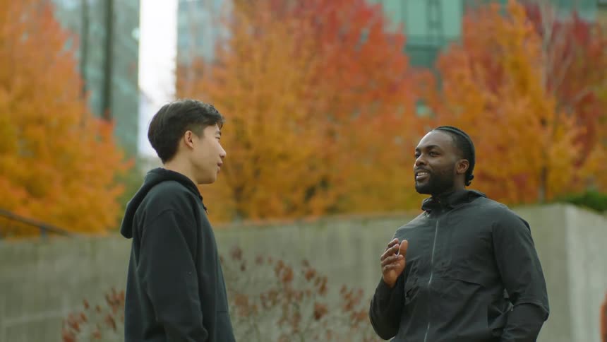 Two men talk to each other in a city with autumnal leaves