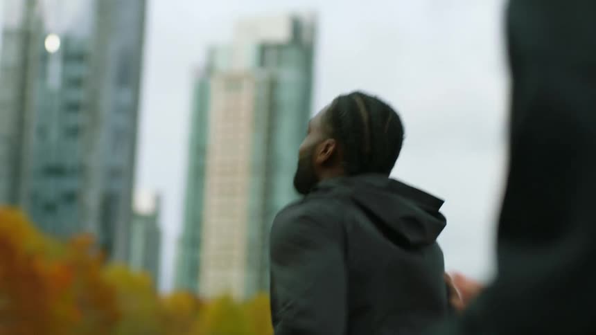 Two young men wearing black sports clothes jogging near the city at fall